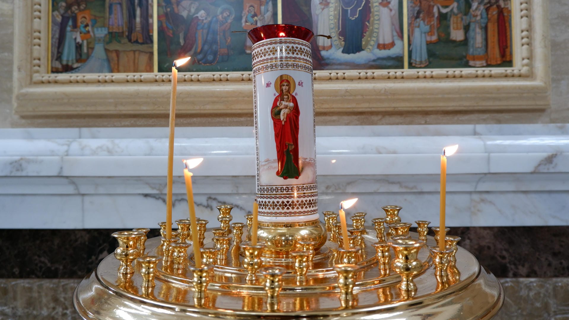 A golden candlestick holds several lit candles, with a religious painting in the background.