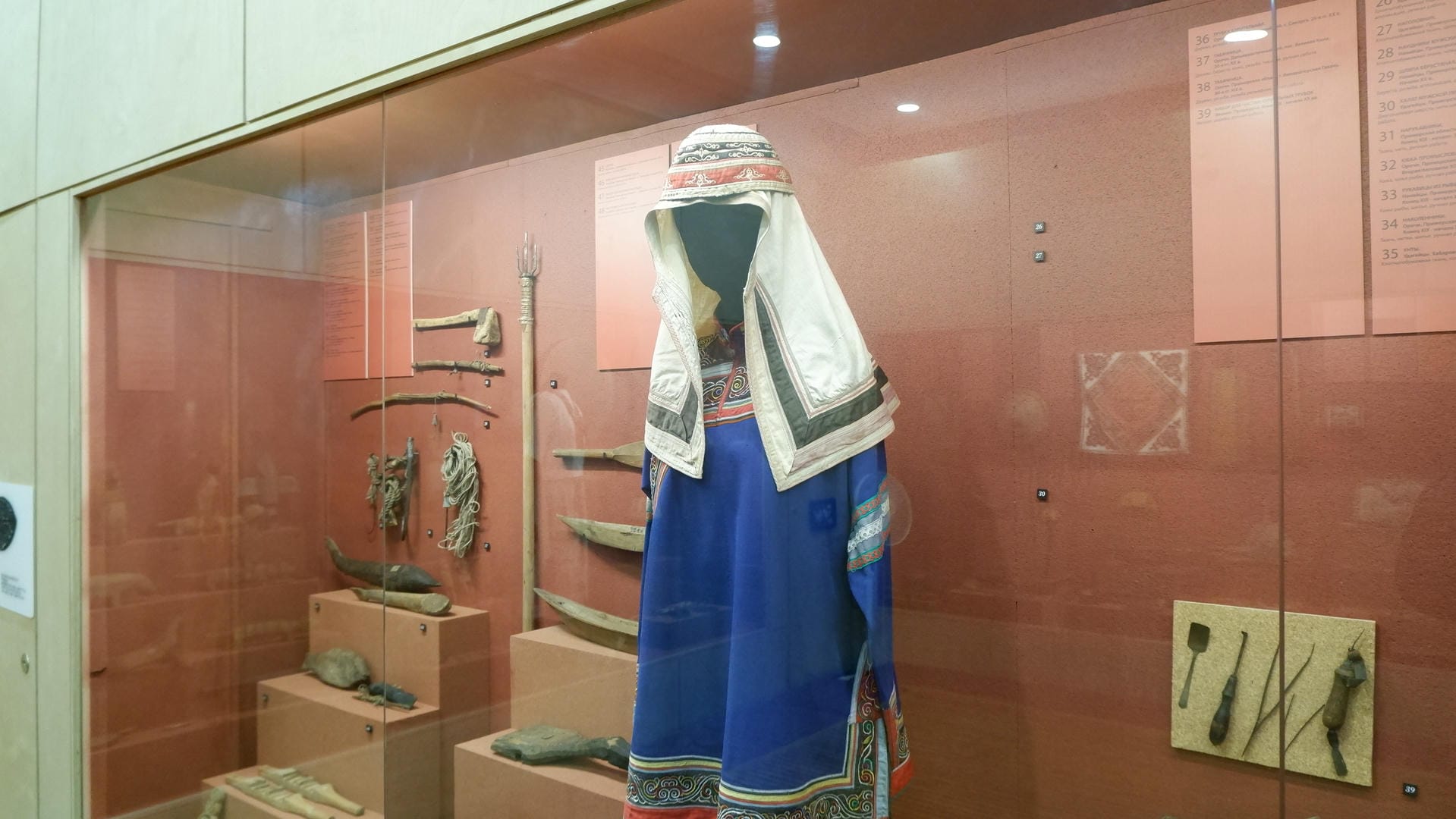 A blue traditional garment hangs in the center of the display case, surrounded by other artifacts.