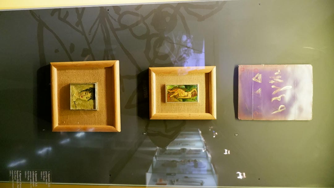 Three small oil paintings: the upper one with a purple background, the middle one featuring a nude female figure, and the lower one a portrait of a woman.