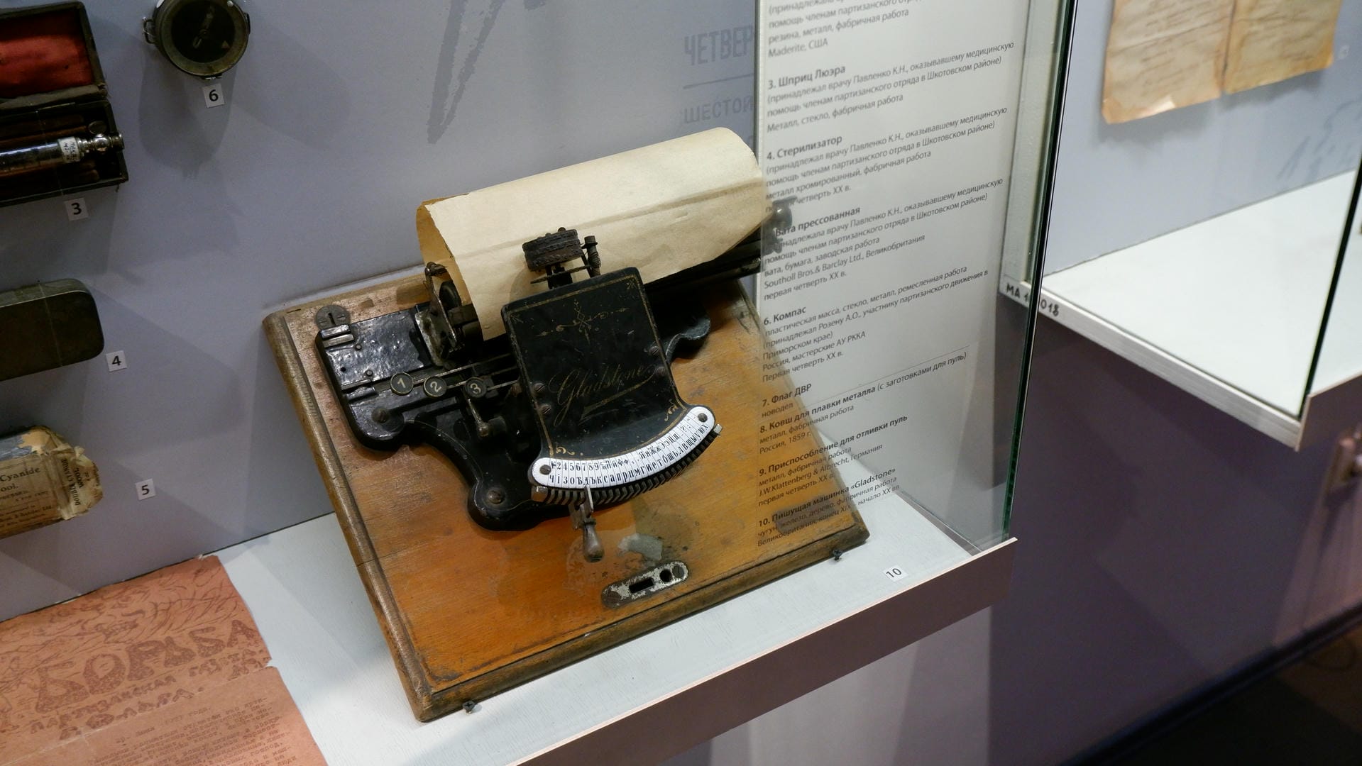 An old typewriter with rolled paper placed inside a glass display case.