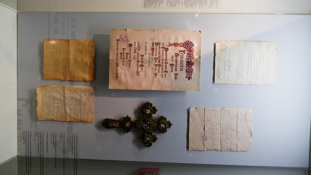 Multiple old documents and a cross displayed in a glass cabinet.