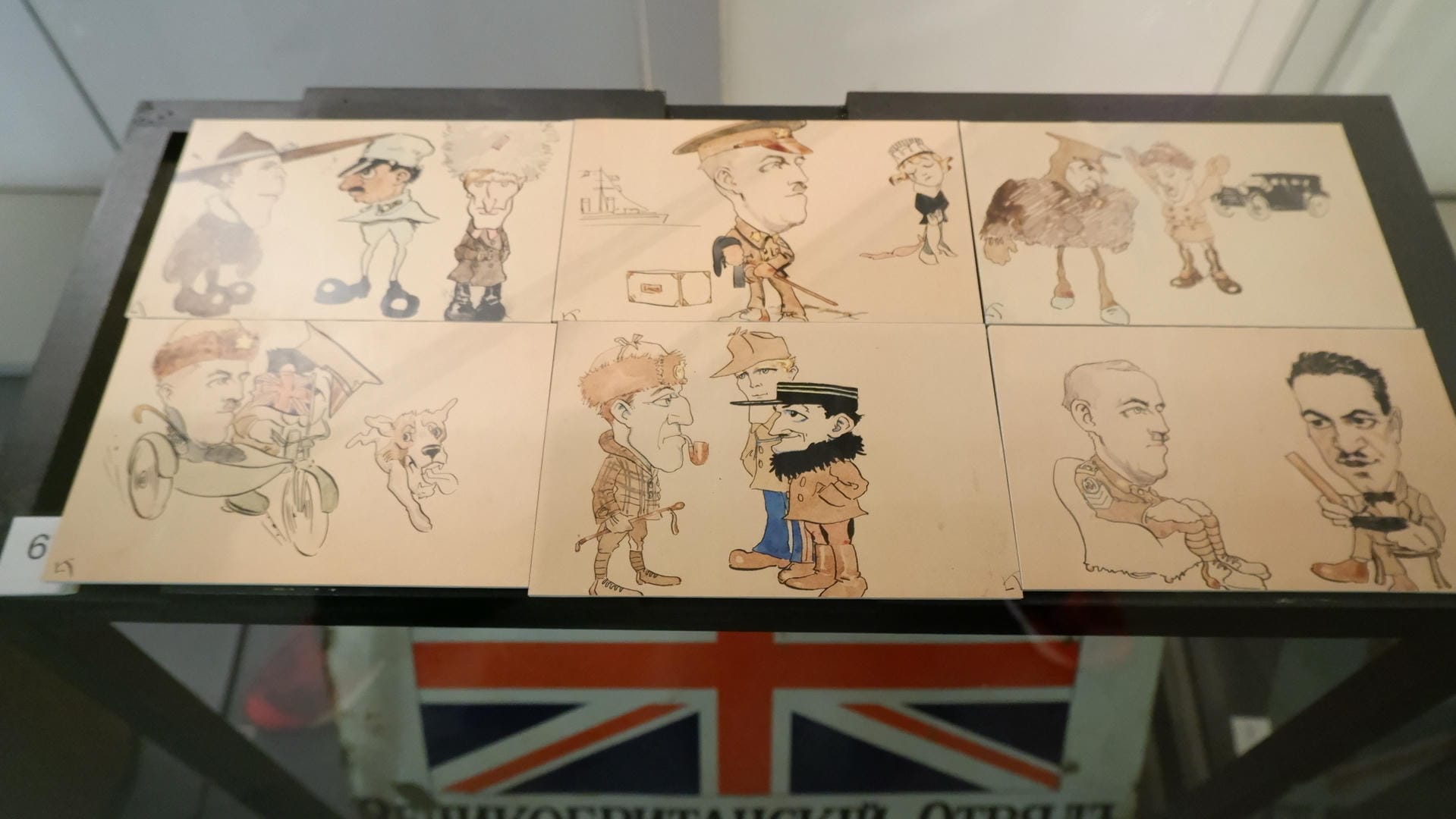 Nine cartoon drawings displayed in a glass cabinet, with a British flag logo below.