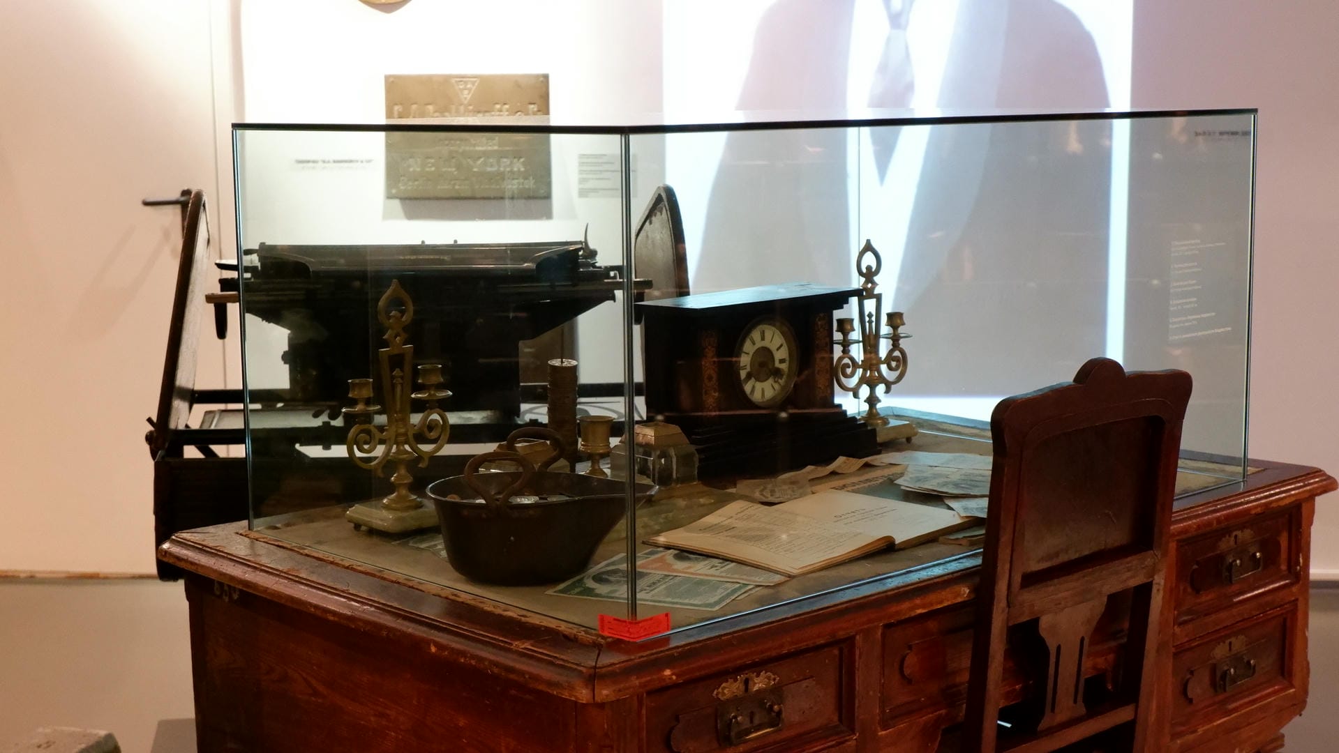 A vintage desk with a typewriter, clock, candlestick, and other items on it.