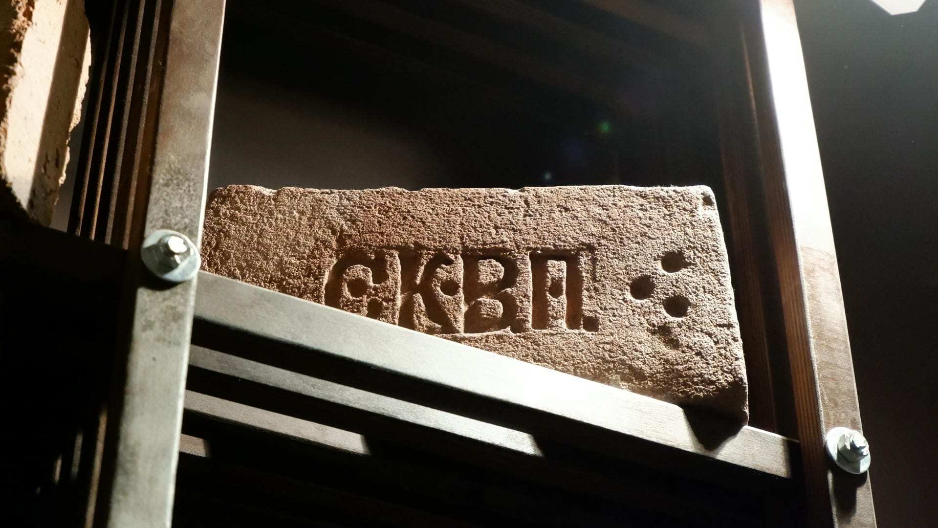 A stone slab engraved with “G.K.B.P.” fixed to the wall with a metal frame.