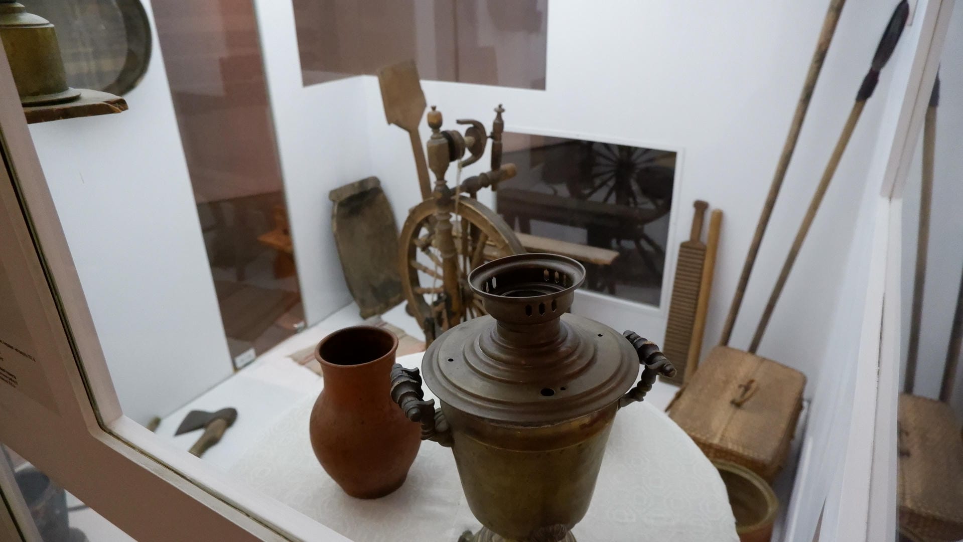 A ceramic pot and a metal container displayed in a glass cabinet, with wooden tools visible in the background.
