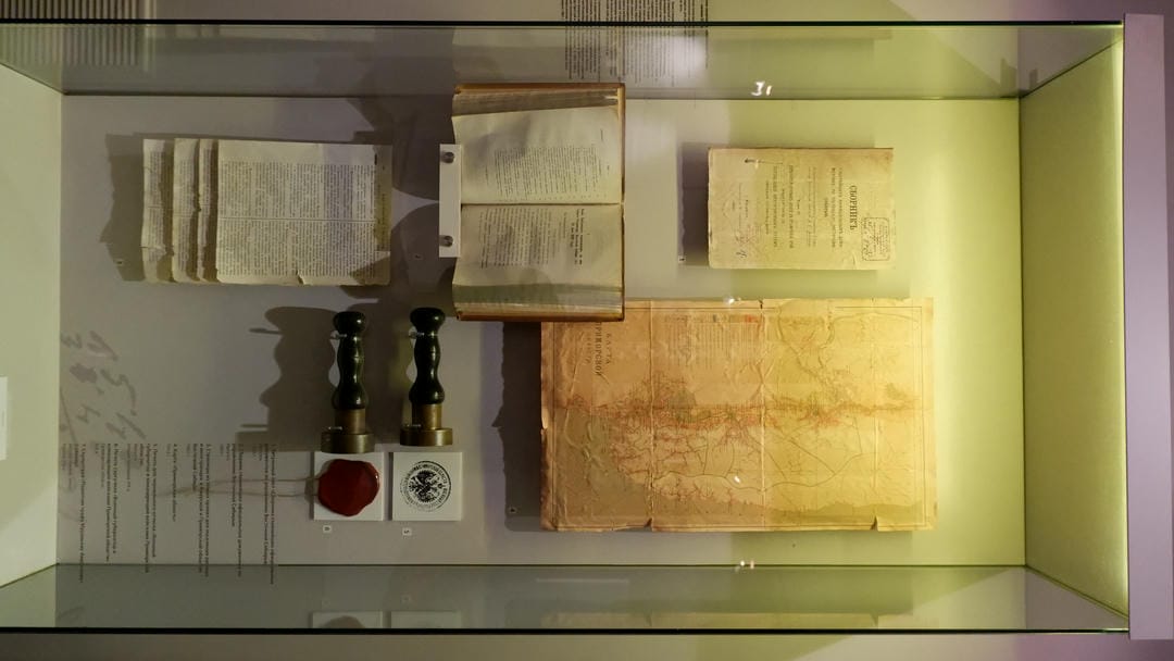 Several old documents, a map, two stamps, and a red wax seal displayed in a glass cabinet.