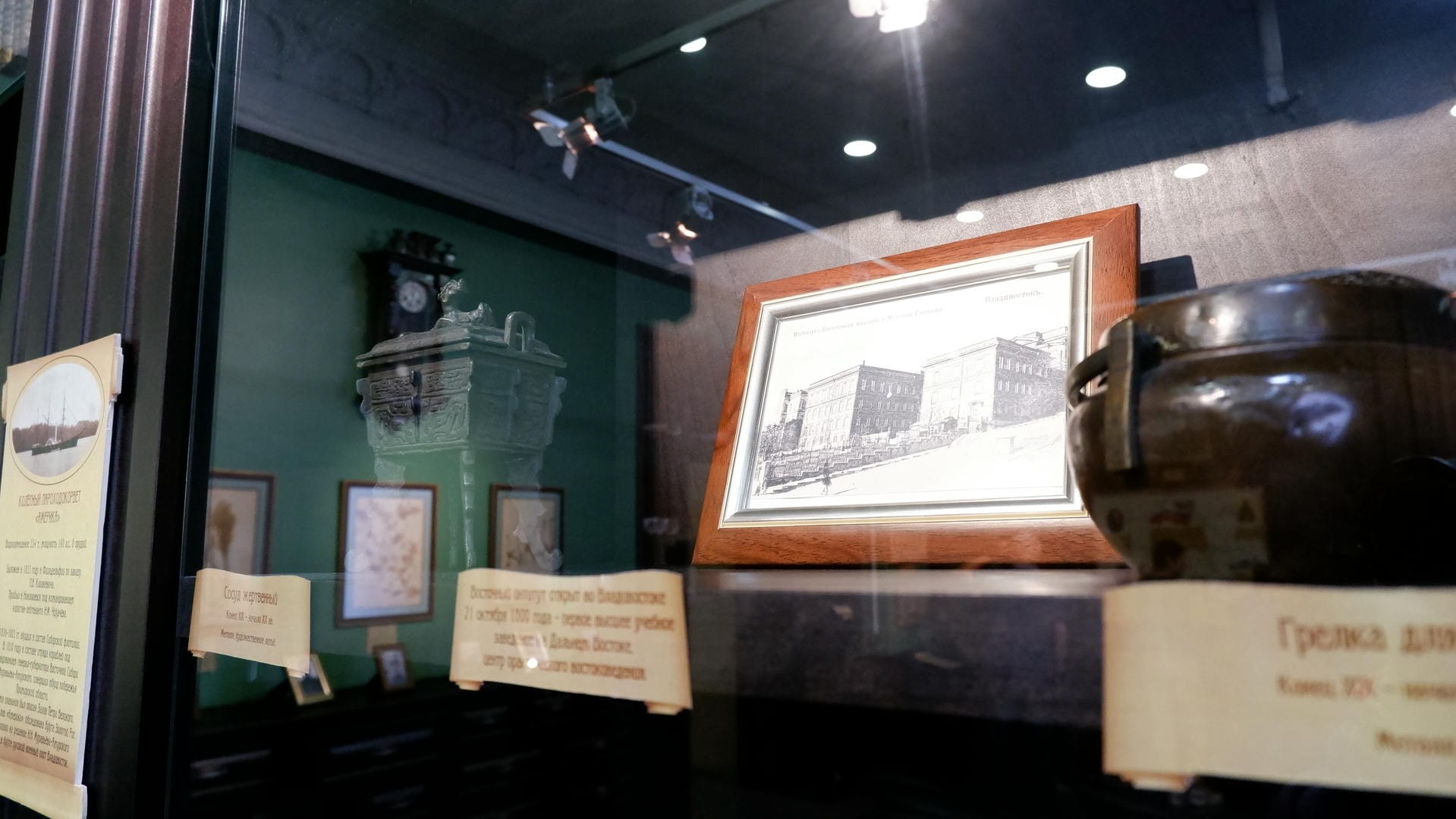 A painting of a building, a green sculpture, and other items displayed in a glass cabinet.