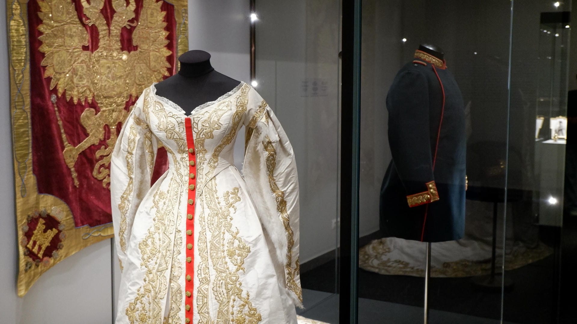 A white dress adorned with gold embroidery, next to a black military uniform.