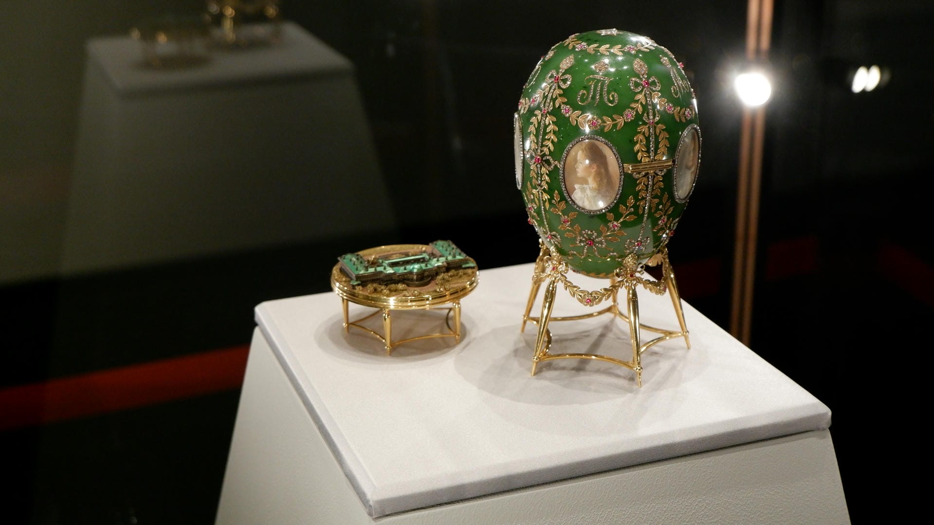 A green Fabergé egg with miniature portraits embedded on its surface, next to a small decorative item.