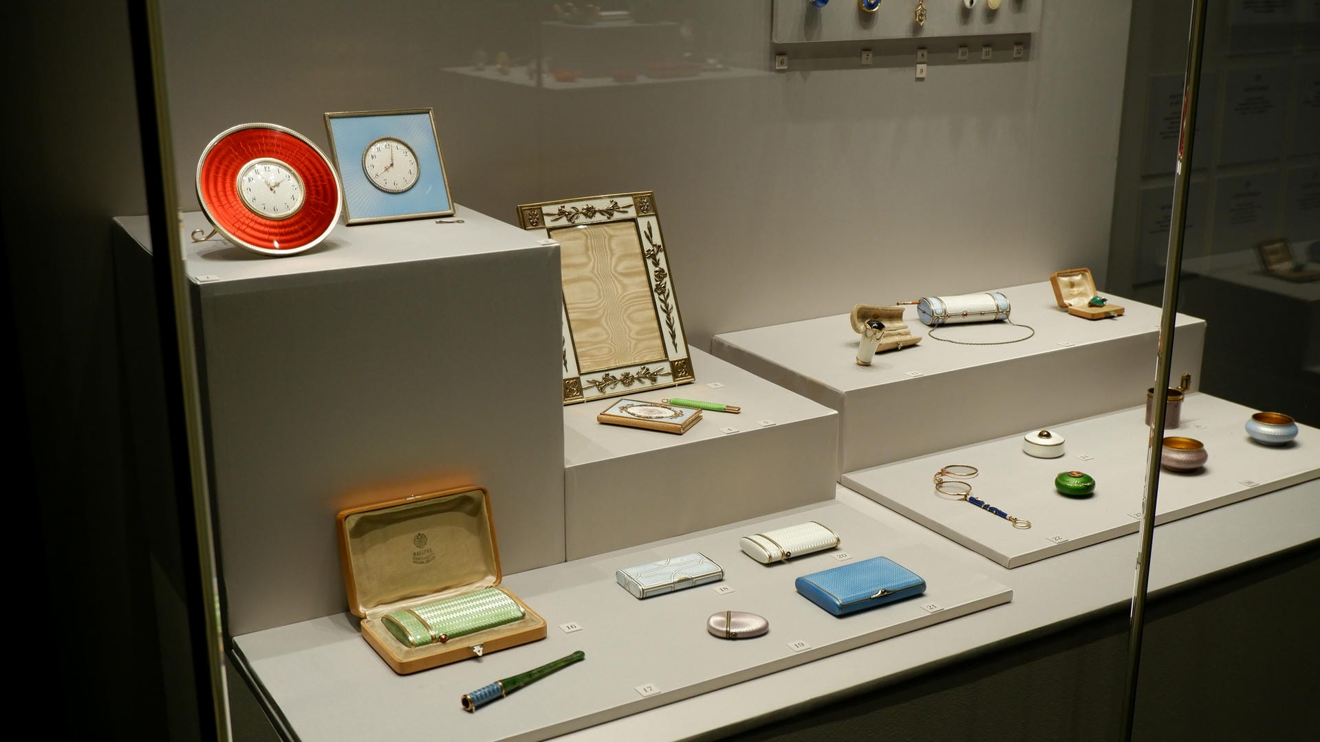 Multiple clocks and jewelry boxes in red and blue colors with intricate patterns displayed in a showcase.