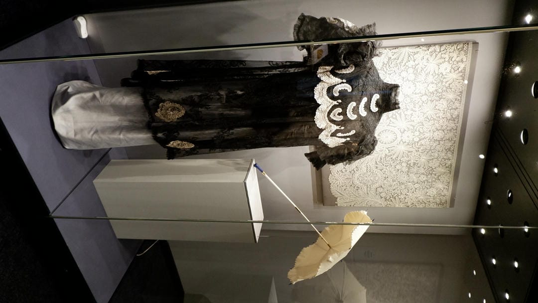 A black lace dress with white embroidery, accompanied by a white parasol.