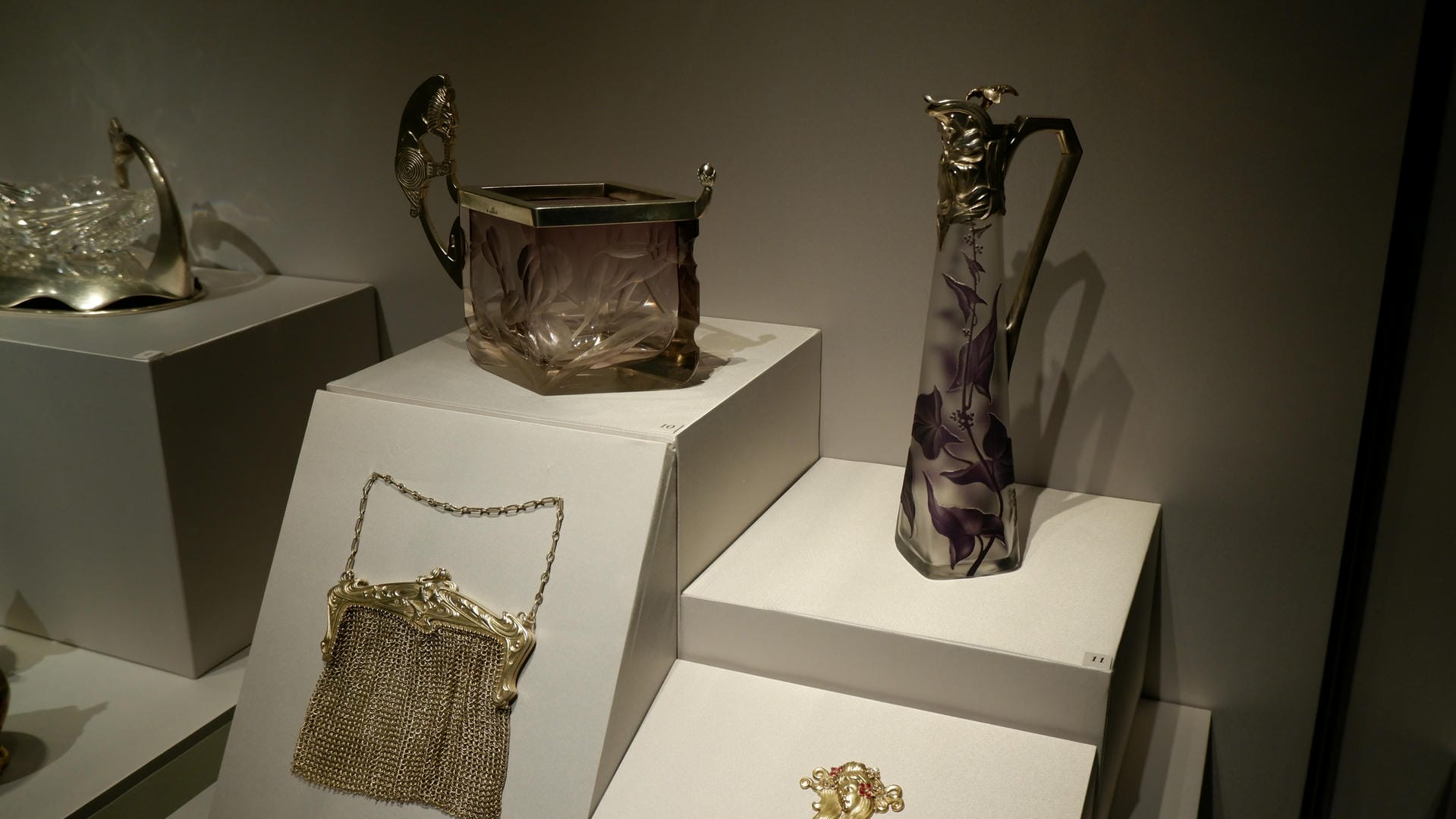 Two goblets with floral patterns and a handbag made of metal chains displayed in a showcase.