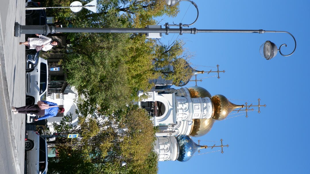 A church with a golden dome surrounded by trees, with two pedestrians in the foreground.