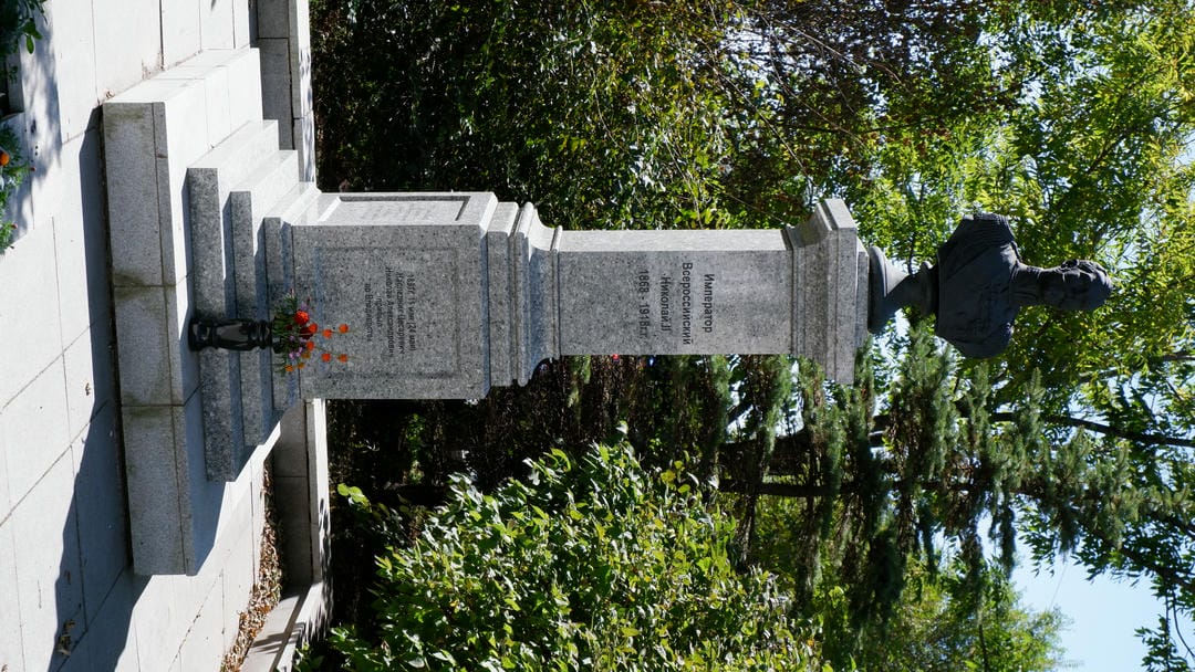 A statue standing on a pedestal with Russian inscriptions, with a bouquet of flowers placed in front.