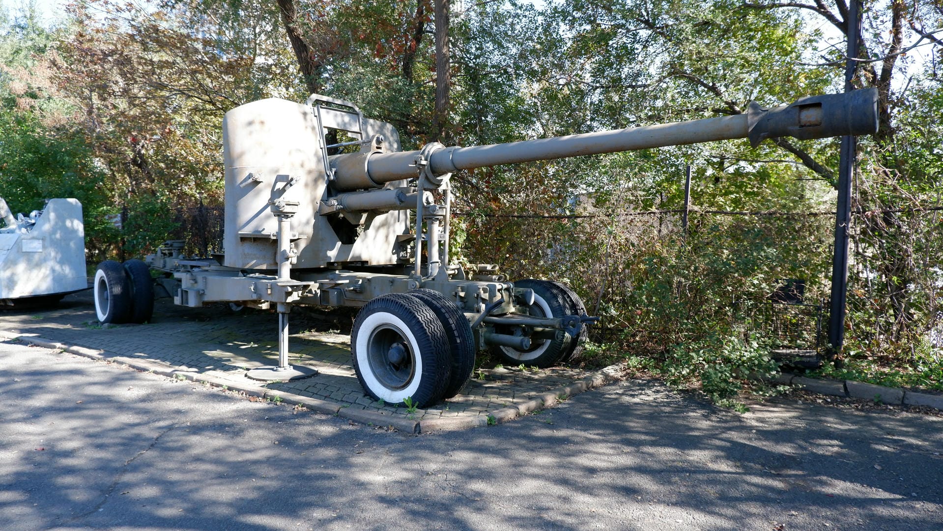 A large cannon installed on a wheeled base, stationed outdoors and surrounded by trees.
