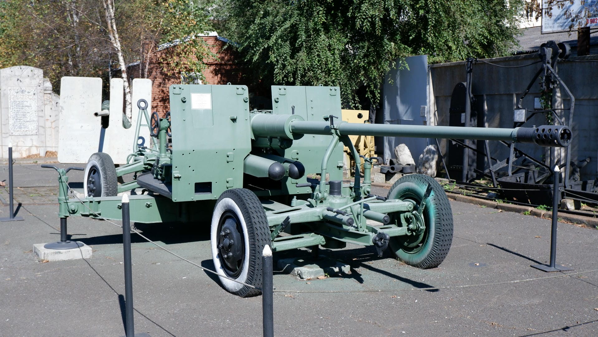 A green cannon installed on a wheeled base, stationed outdoors and surrounded by stone monuments.