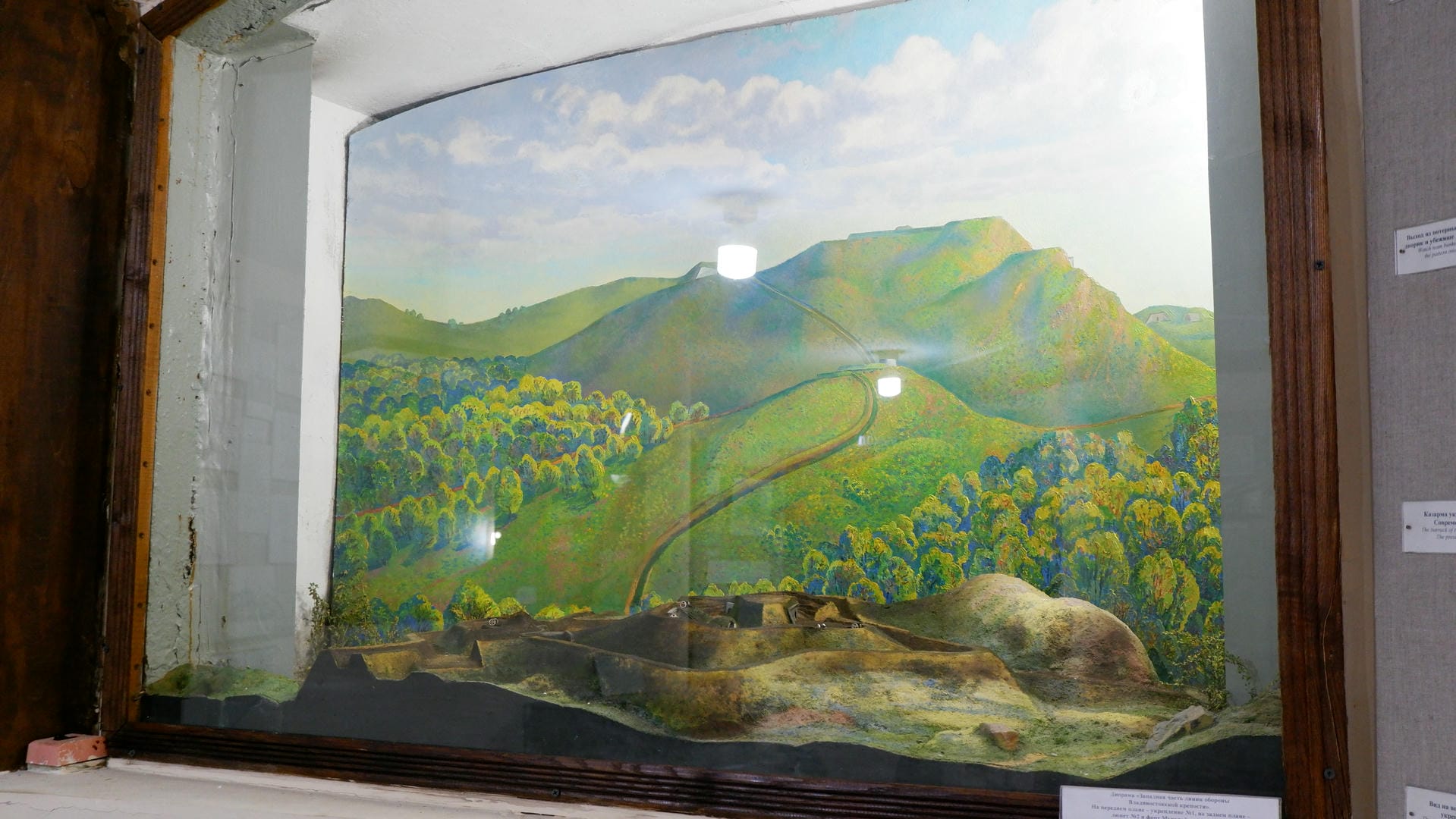 A painting depicting green hills and forests, with model terrain in the foreground.