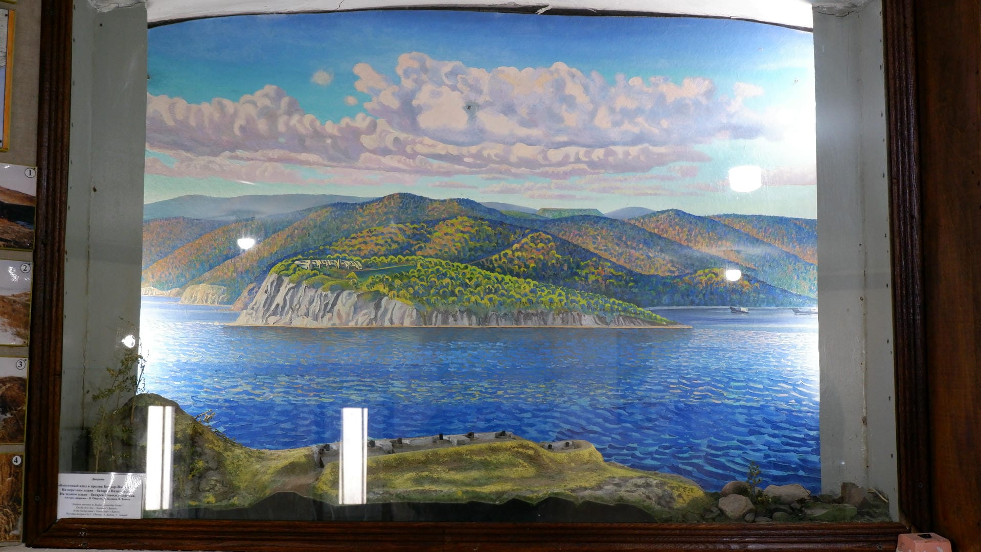 A painting depicting a lake and mountains, with clouds in the sky and model terrain in the foreground.