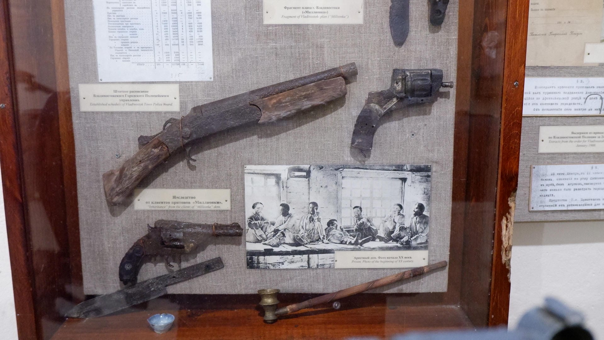 A display case contains old weapons, including a long gun, a short gun, and a knife, next to an old photo.