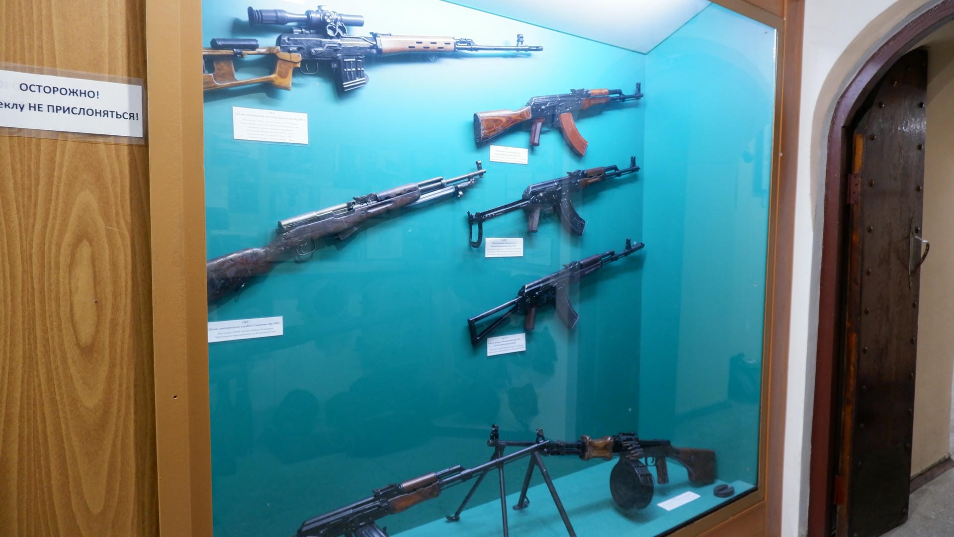 A display case exhibits various firearms, including rifles and machine guns, each labeled underneath.