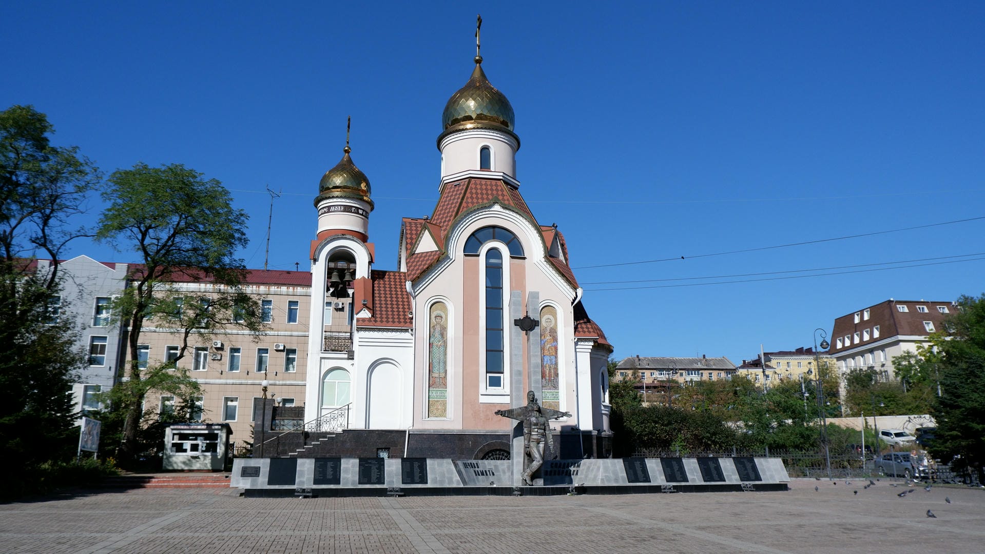 A church with a golden dome, a statue in front, surrounded by a square and buildings.