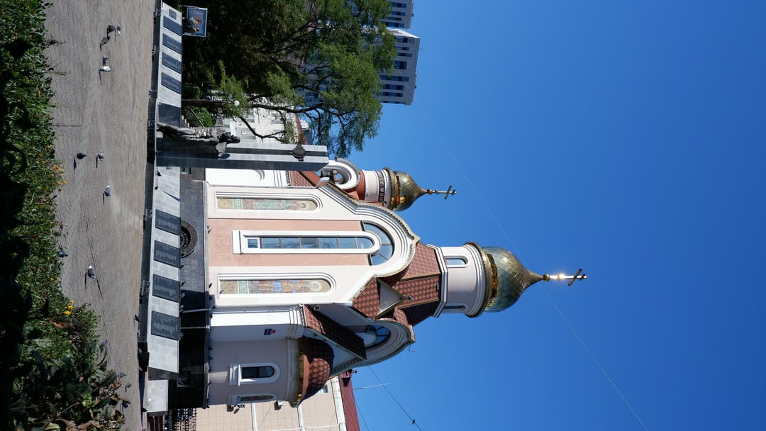 A church with a golden dome, a statue in front, surrounded by a square and buildings.
