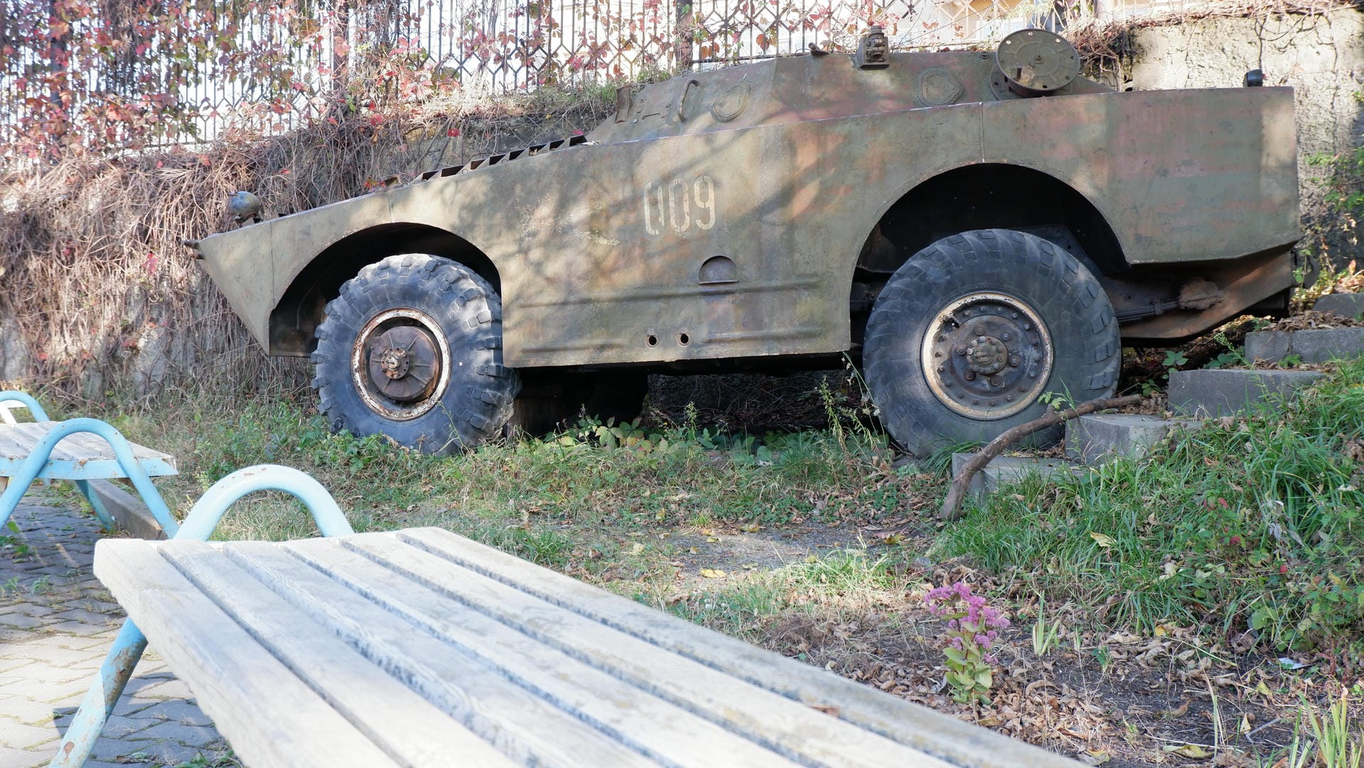 An old armored vehicle parked on the grass, with several benches nearby.