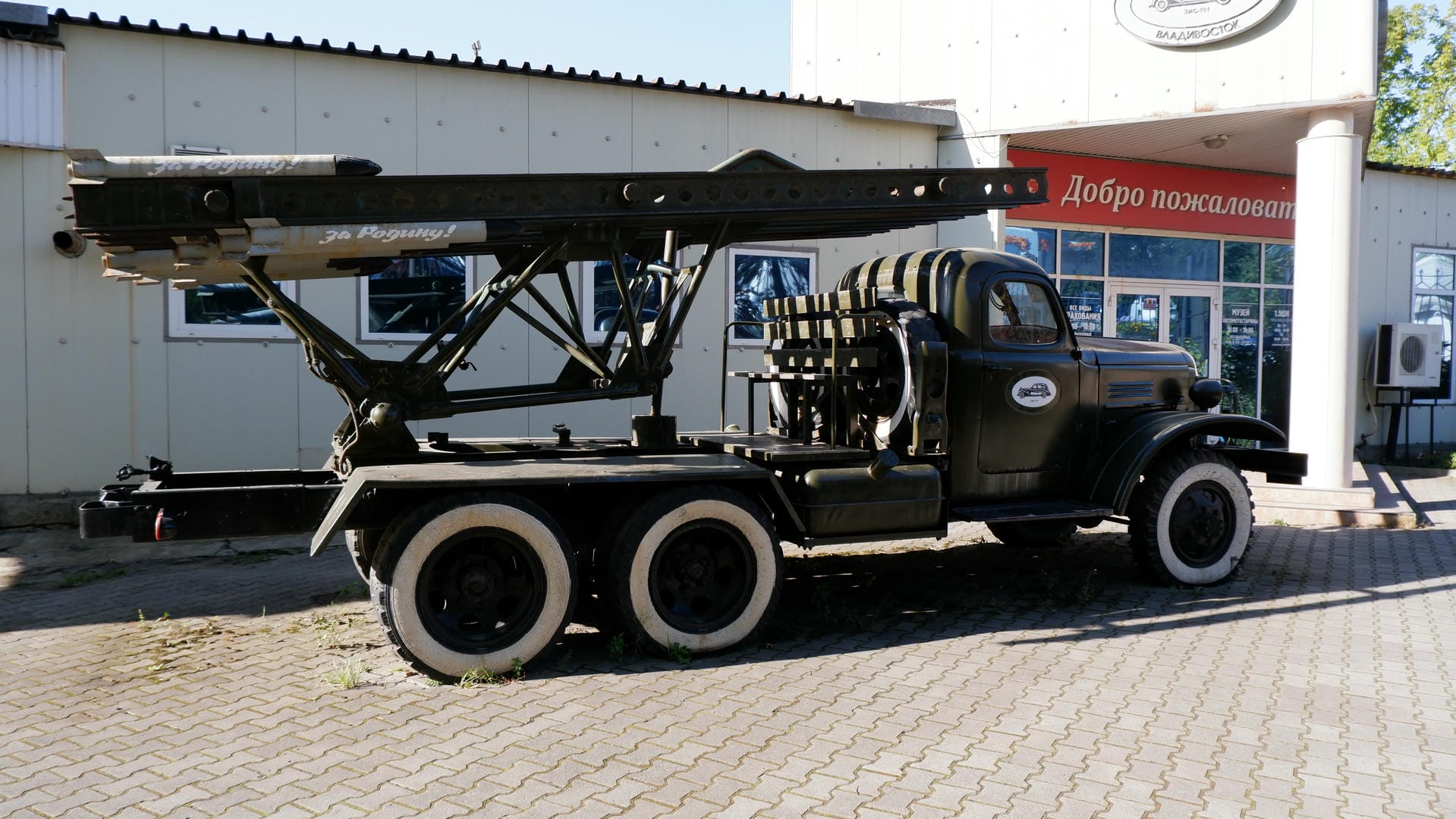 A black military truck parked in front of a building, equipped with rocket launchers.