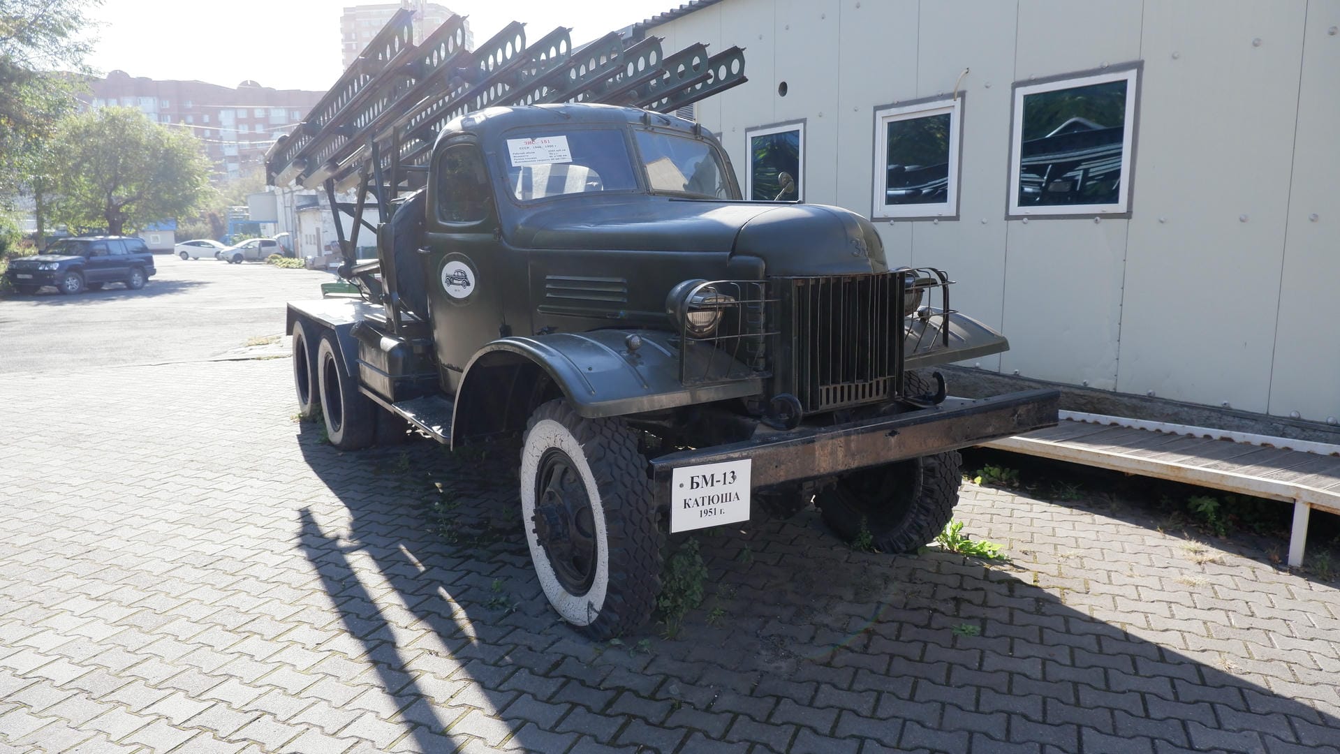 A black military truck parked in front of a building, with license plate БМ-13 КАТЮША 1951г.