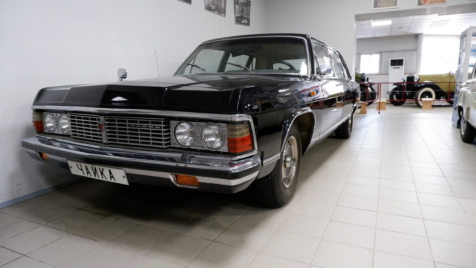 A black luxury car parked inside an exhibition hall, with license plate ЧАЙКА.