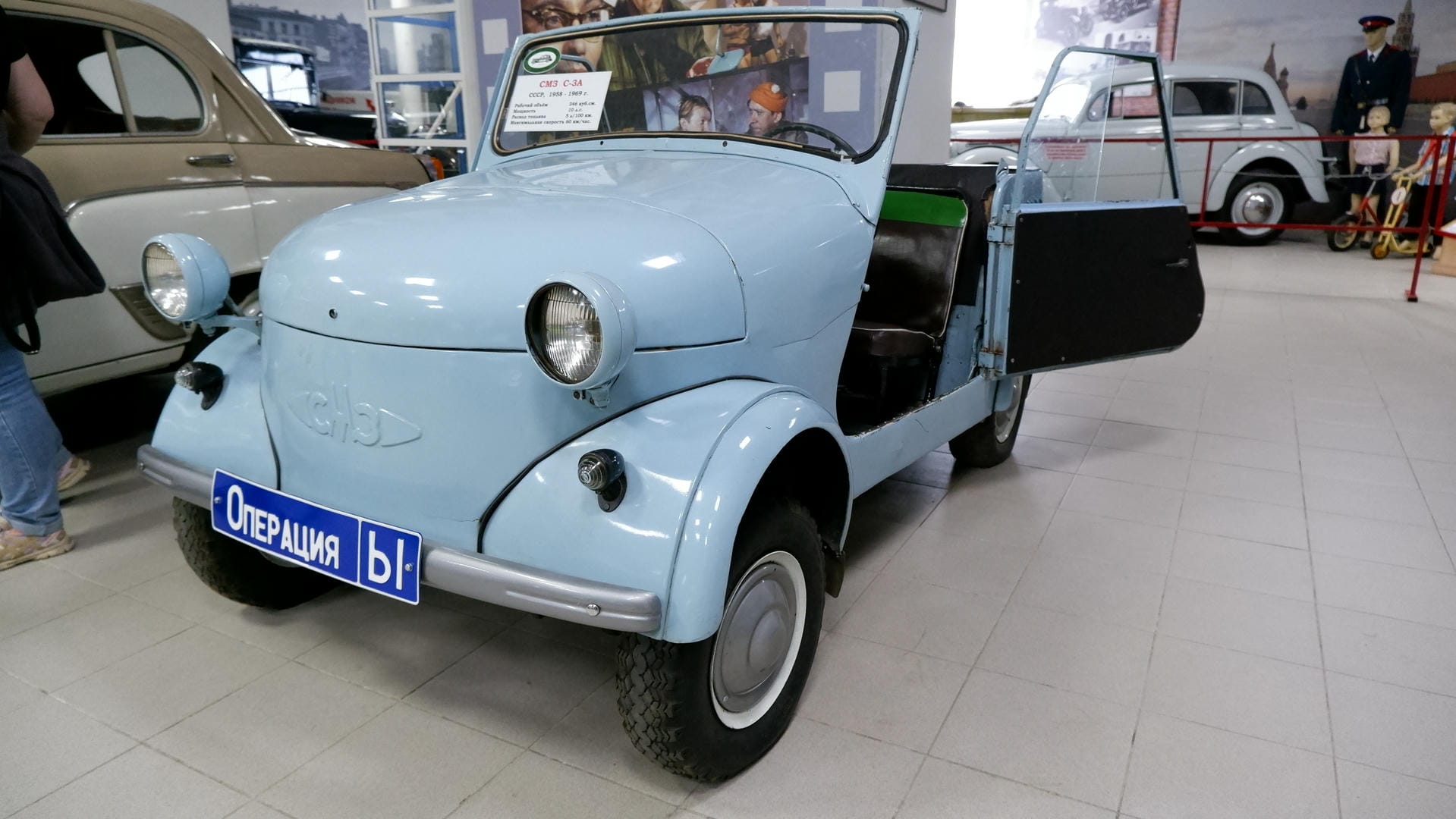 A light blue small retro car with the door open, license plate reading “ОПЕРАЦИЯ ы.”