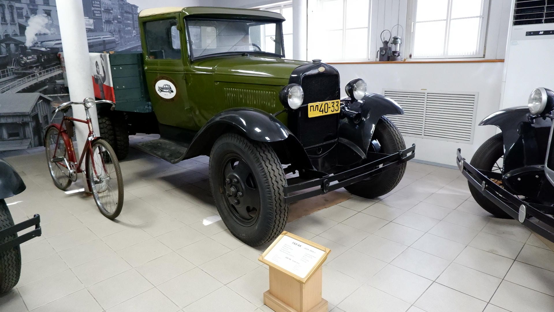 A green vintage truck with license plate “пл40-33,” parked next to a red bicycle.