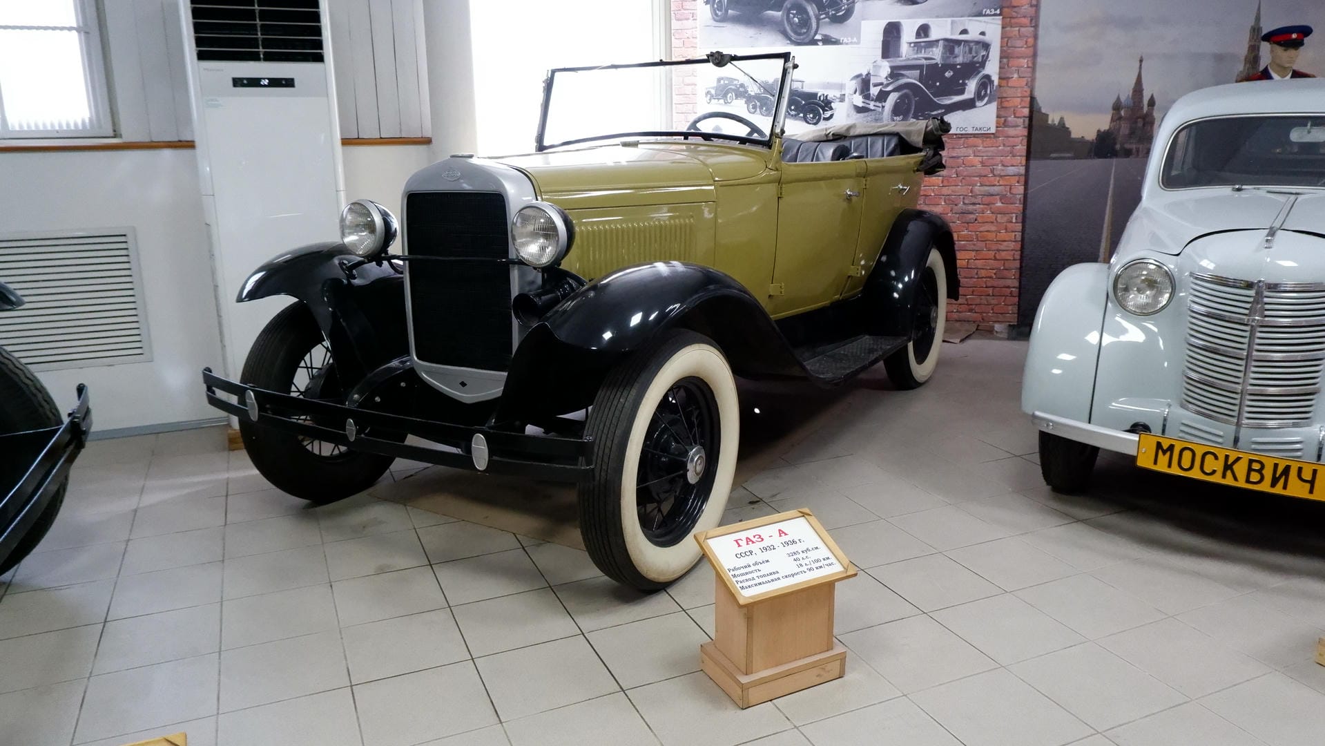 A yellow and black open-top vintage car with license plate “ГАЗ - А,” next to a wooden signboard.