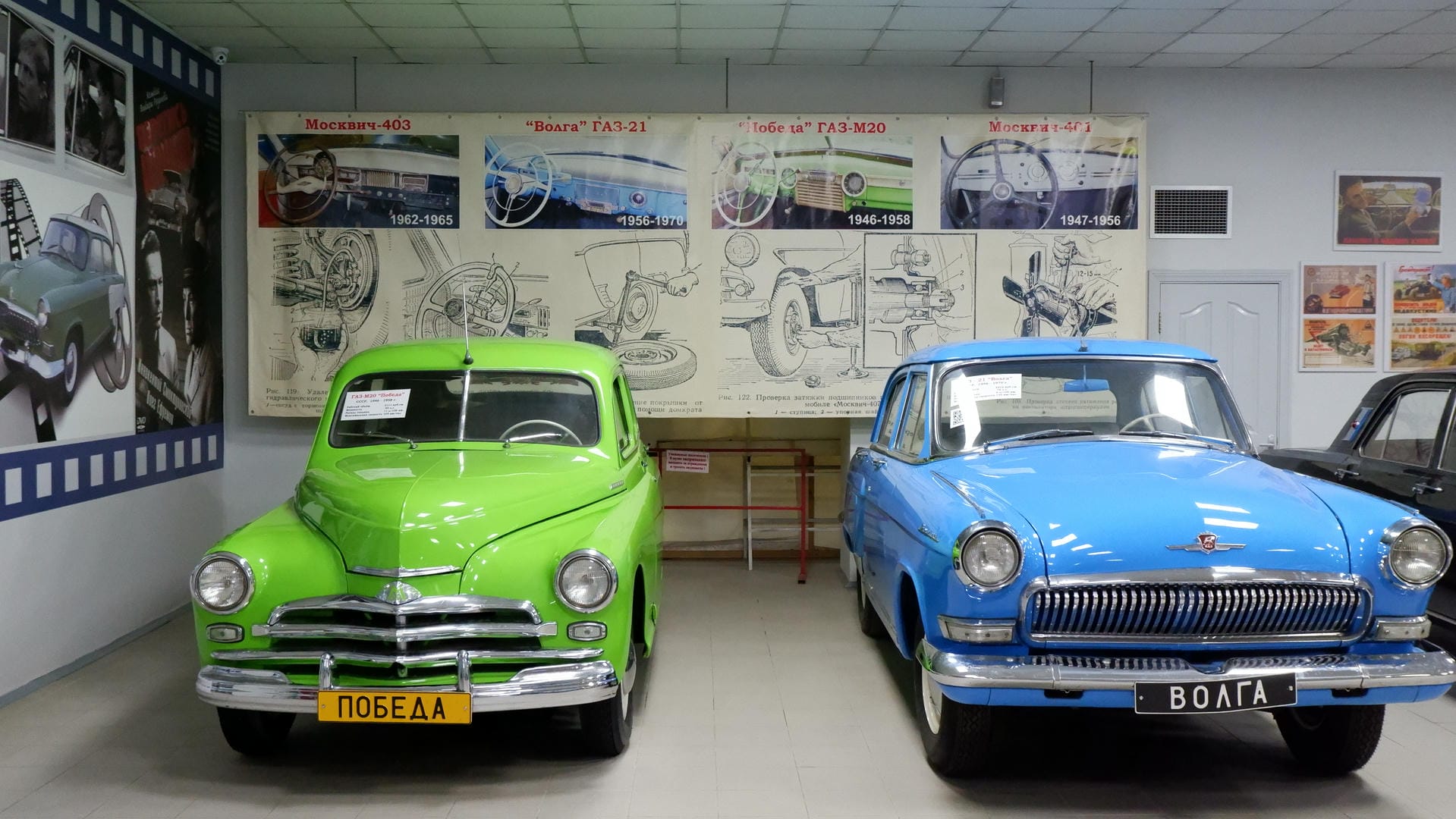 A green and a blue vintage car parked side by side, with various car blueprints displayed on the background wall.