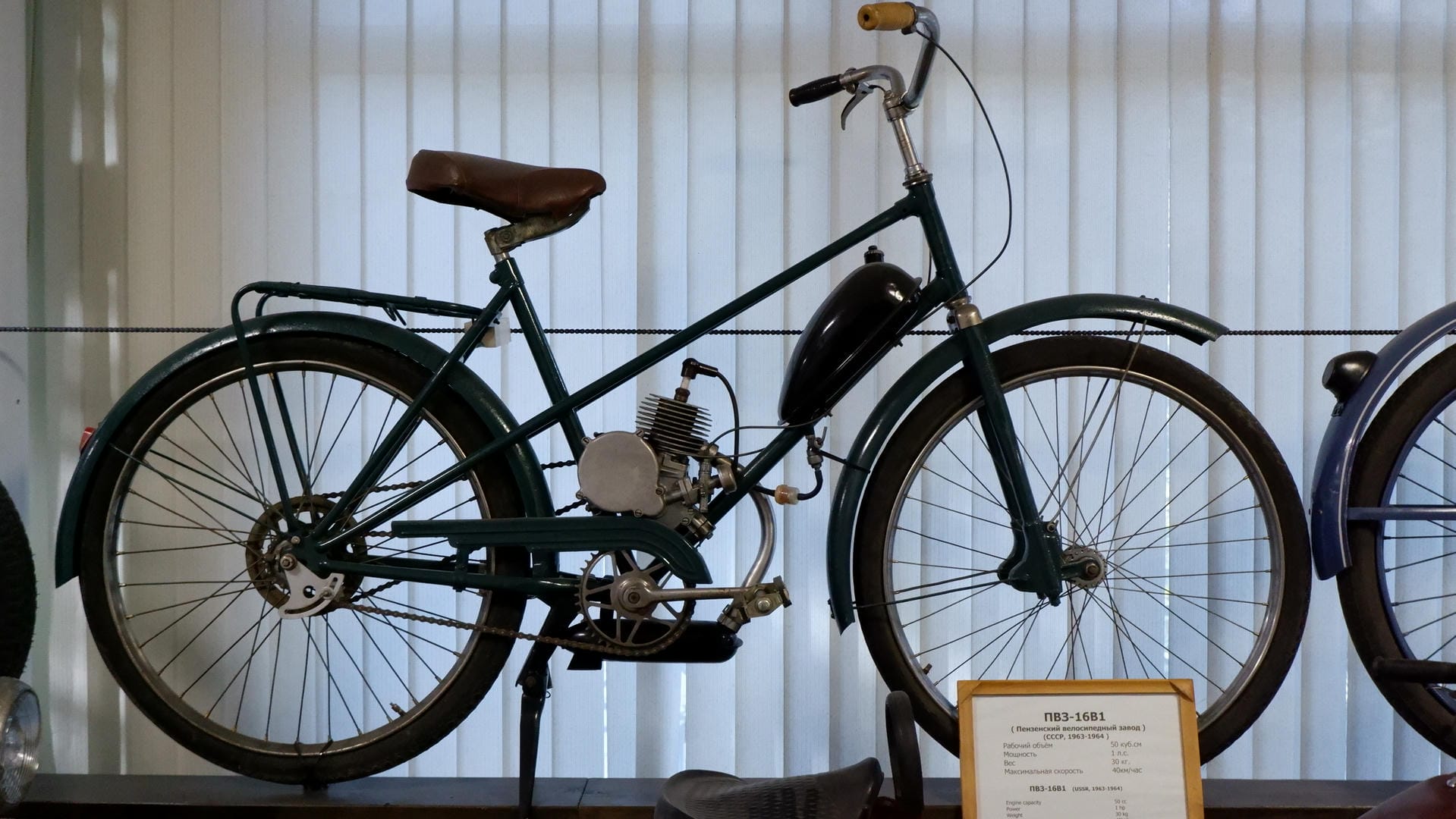 A green bicycle with an engine device on the frame and a brown seat.