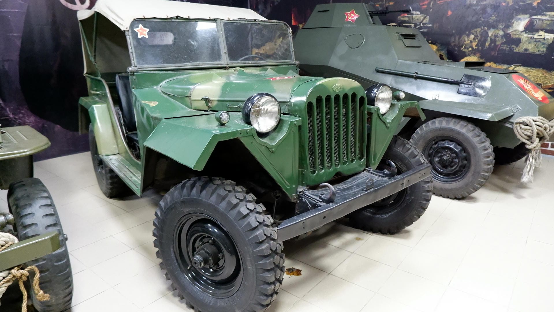 A green military vehicle with a red star emblem on the front, next to an armored vehicle.