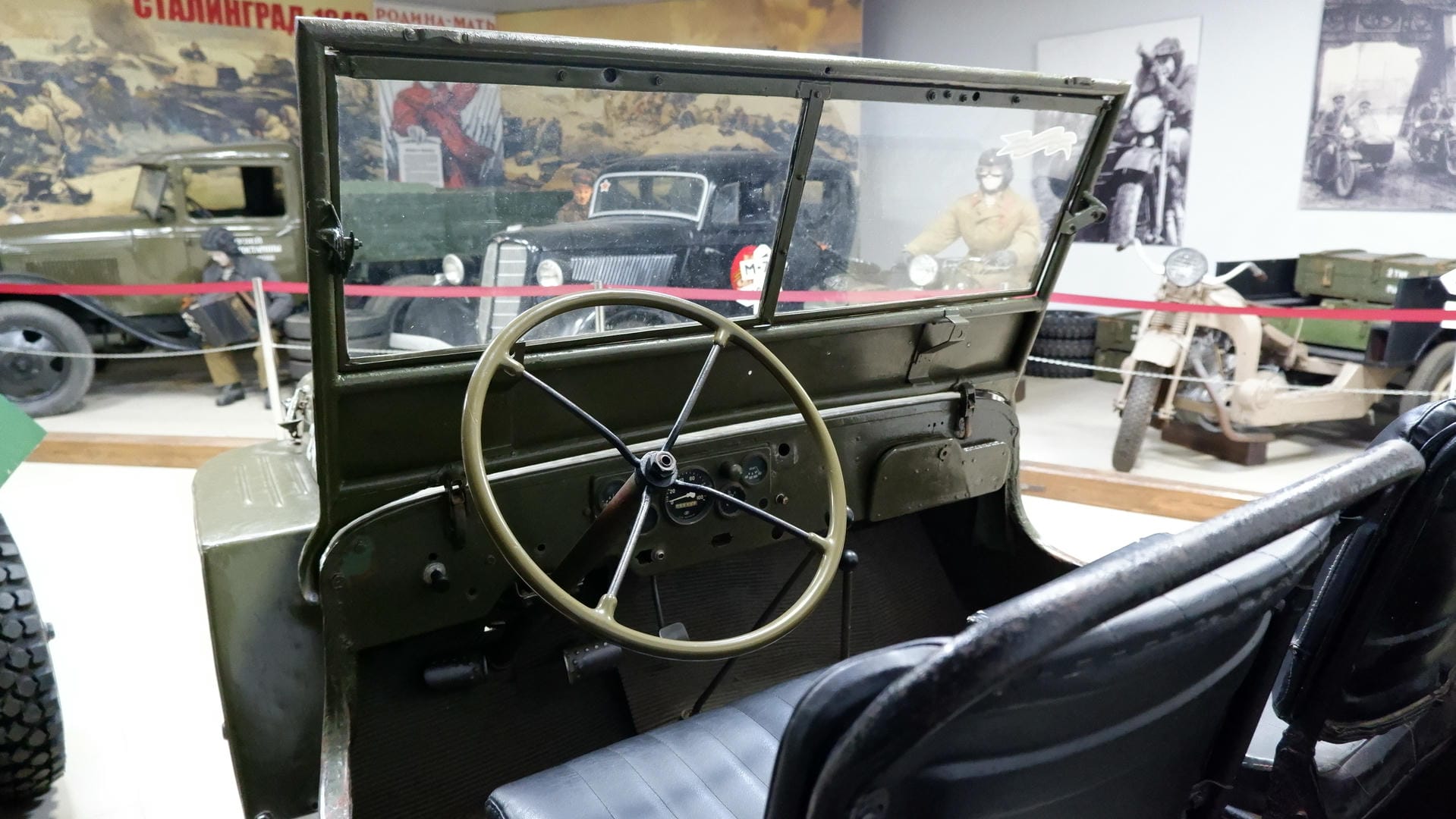The interior of a military vehicle with the steering wheel on the left, black leather seats, and an instrument panel ahead.