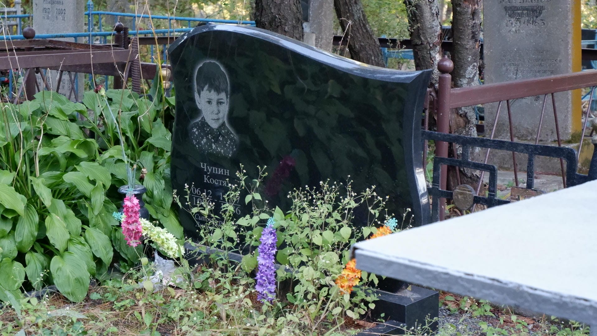 A tombstone engraved with a young boy’s photo and name, surrounded by flowers.