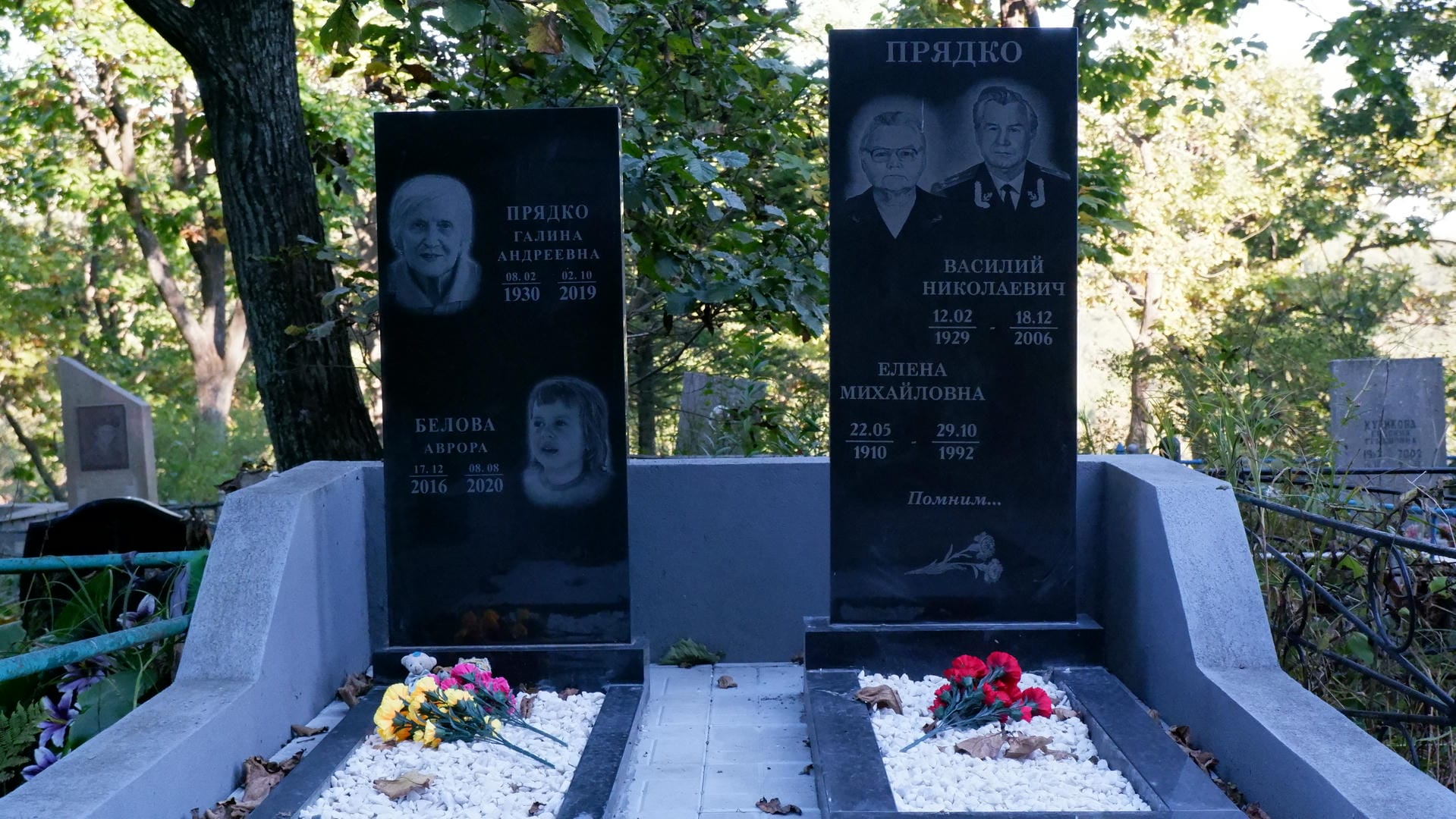 Two tombstones engraved with photos and birth-death years of Pradko family members, with flowers placed beside them.