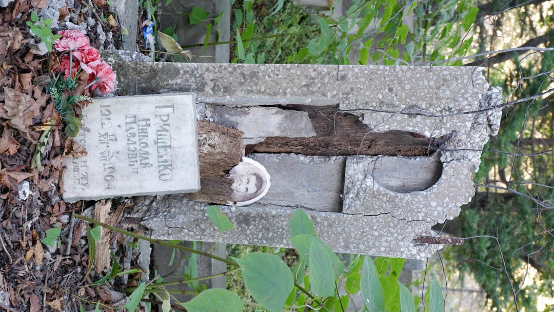 A severely damaged tombstone with a circular depression in the middle and a small stone slab engraved with text below.