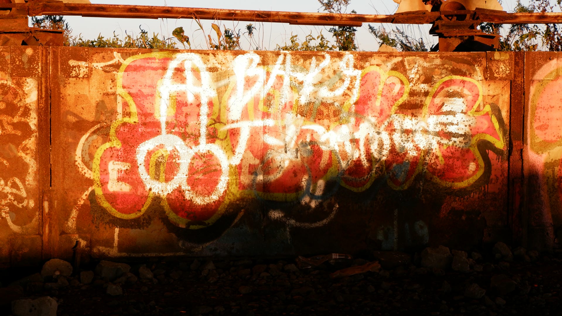 A wall covered in colorful graffiti, with a rusty metal plate in the background.