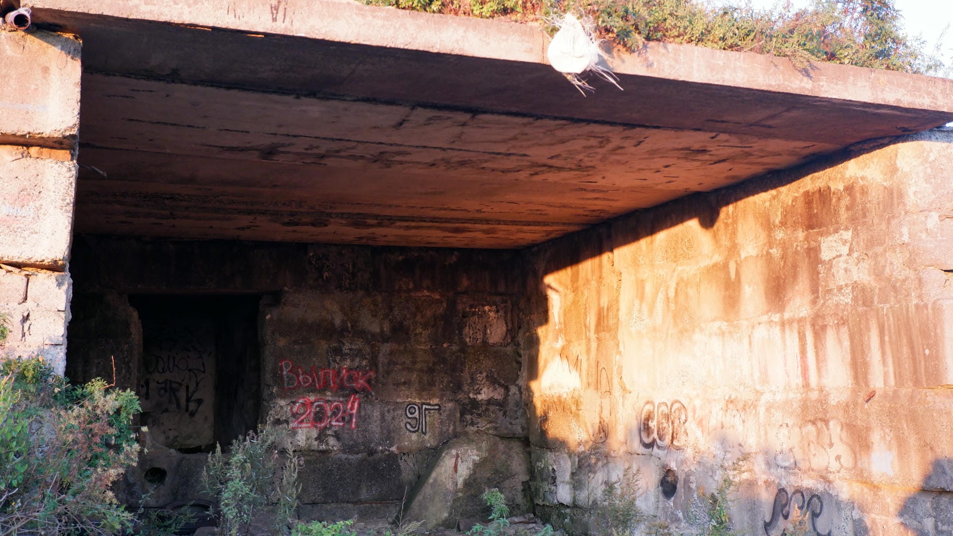 An abandoned concrete structure, with red graffiti on the walls and a white plastic bag hanging from the top.