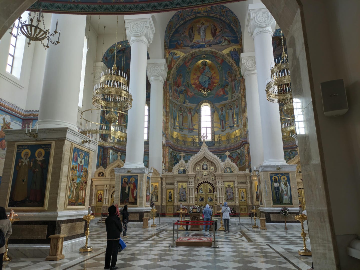 The interior of the church is lavishly decorated, with golden murals and chandeliers, while worshippers pray.