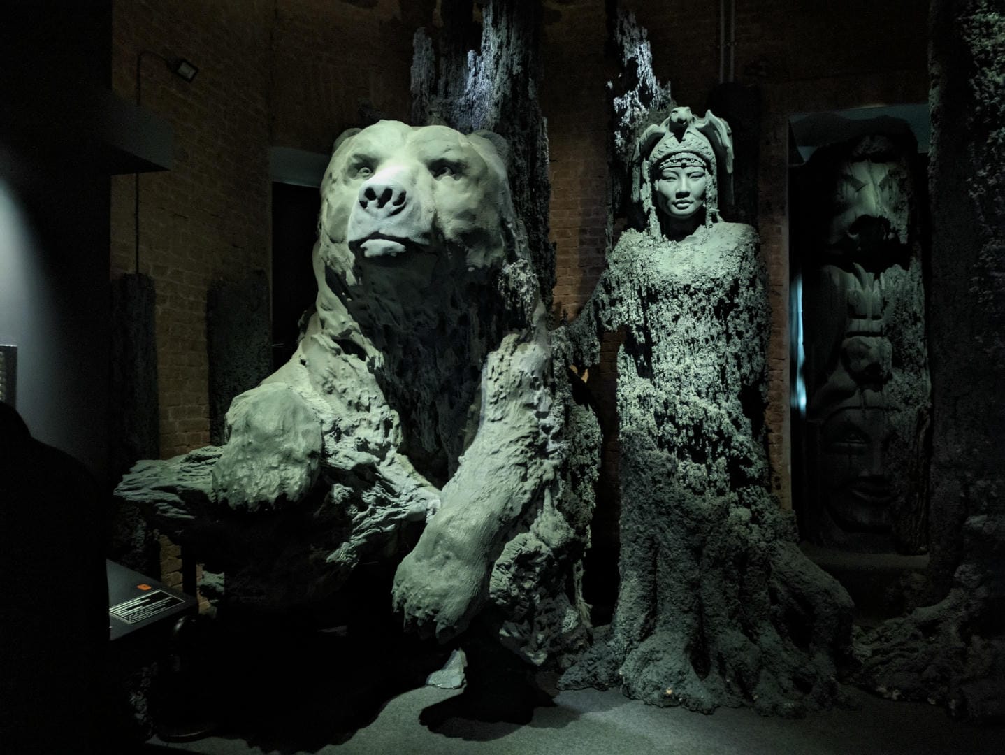 A bear and a human-shaped sculpture displayed side by side, with a rough surface.
