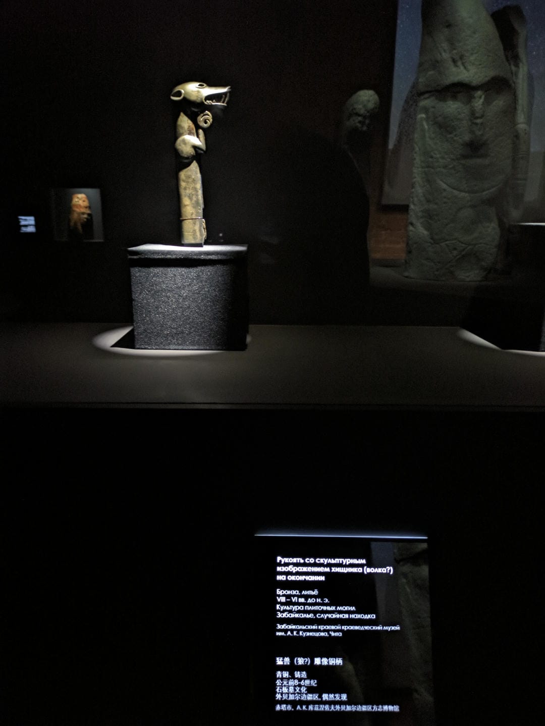 An animal statue with a wolf-like head, slender body, short limbs, and a dark background.