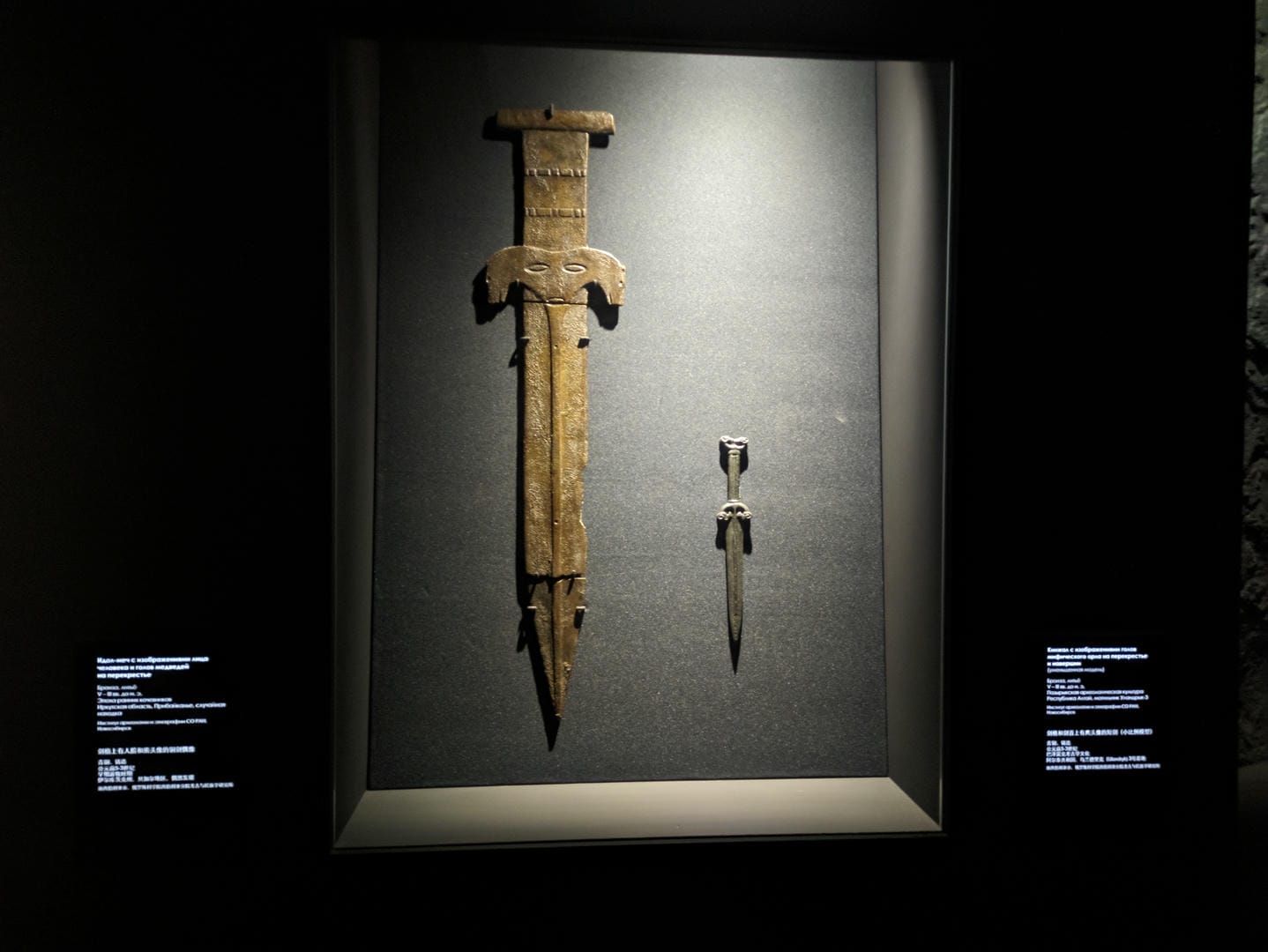 Two swords, one longer and the other shorter, with carved patterns on the handles, against a black background.