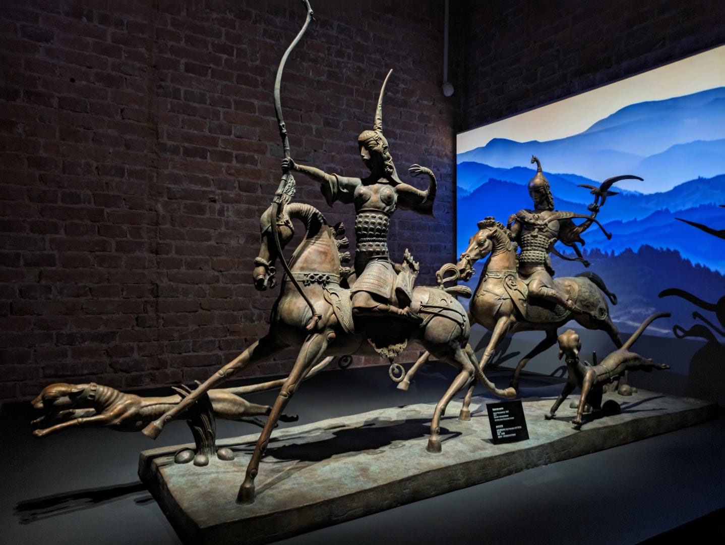 Two equestrian statues, the front figure holding a bow and arrow, the rear figure holding a weapon, with a mountain landscape painting in the background.