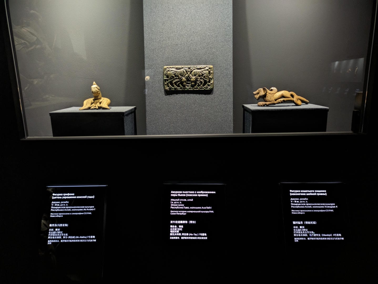Two animal statues and a decorative panel: a crouching animal on the left, a decorative panel in the middle, and a lying animal on the right, against a gray background.