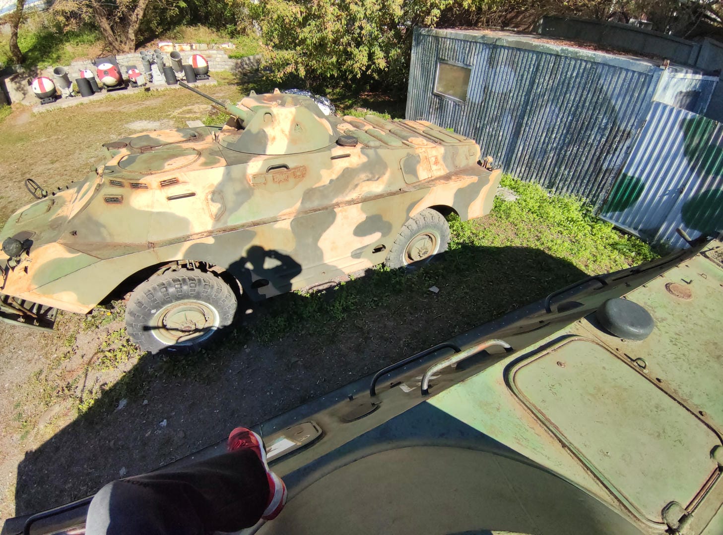 An armored vehicle parked outdoors with mottled green and brown camouflage patterns on its body.