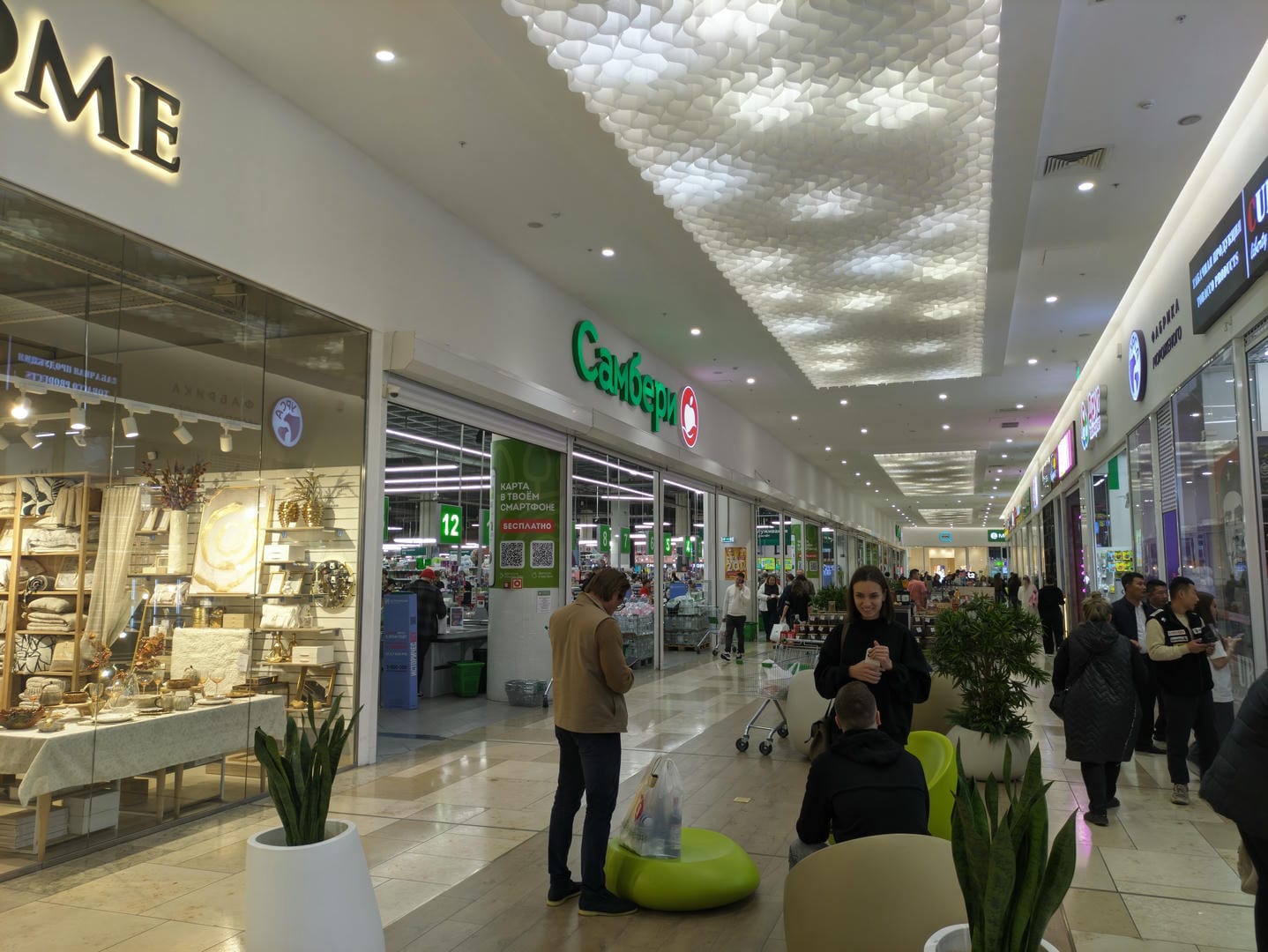 Inside a mall, the ceiling is decorated with honeycomb patterns, and customers are shopping and resting.